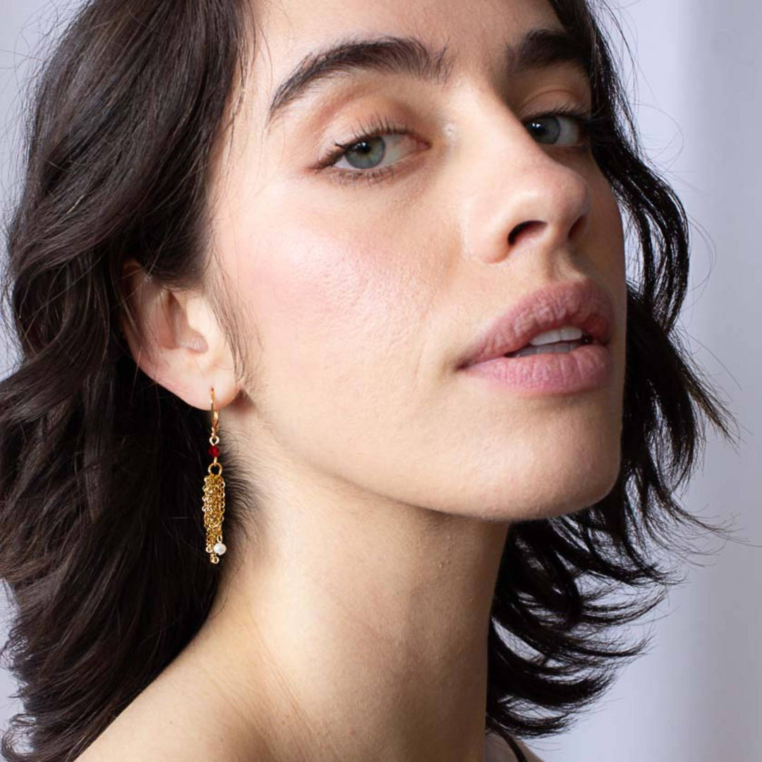 Femme portant une Boucle d'oreilles Dafio dorées par Anne-Marie Chagnon avec chaînes, perles et bille rouge