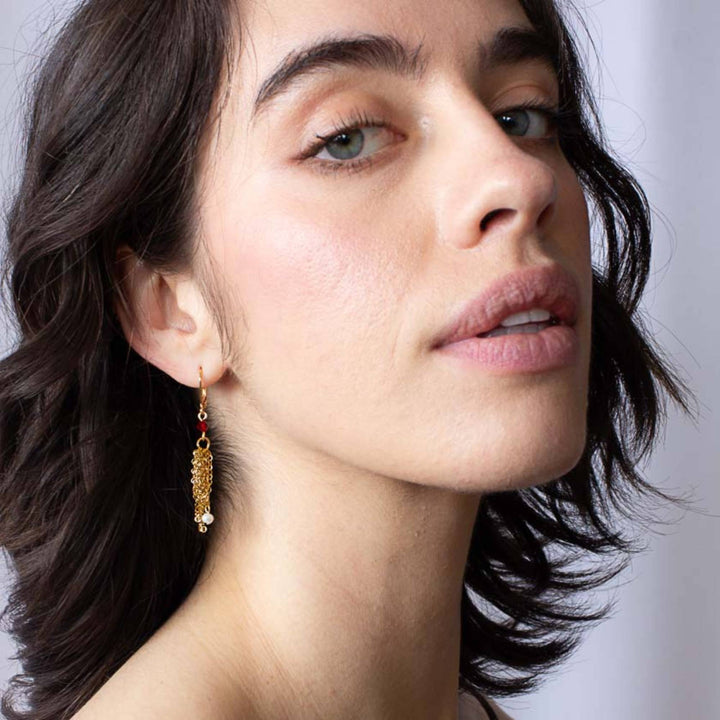 Femme portant une Boucle d'oreilles Dafio dorées par Anne-Marie Chagnon avec chaînes, perles et bille rouge
