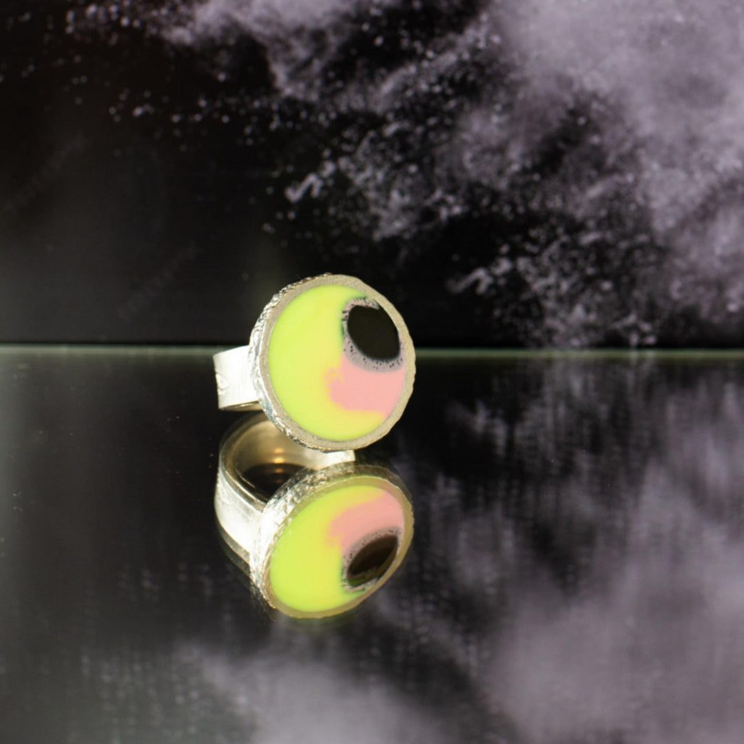Bague Wilfred jaune, rose et noire par Anne-Marie Chagnon déposée sur le sol avec fond noir et gris