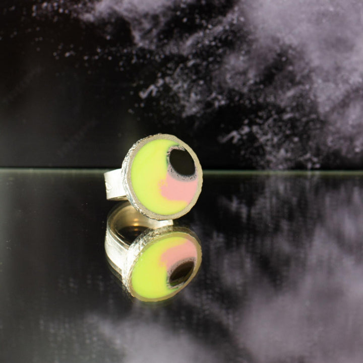 Bague Wilfred jaune, rose et noire par Anne-Marie Chagnon déposée sur le sol avec fond noir et gris