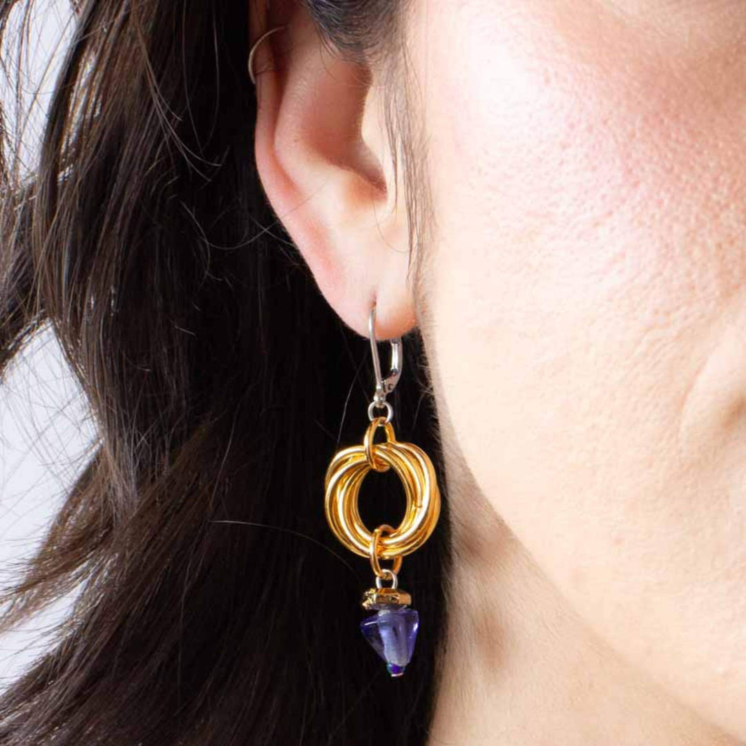 Femme portant des Boucles d'oreilles Anne-Marie Chagnon Jilka avec crochets argentés, anneaux dorés et pierre triangulaire mauve suspendue