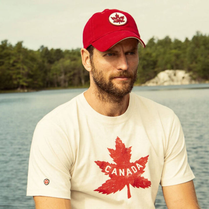 Homme avec un lac en arrière plan portant une Casquette Canada rouge avec logo par Red Canoe