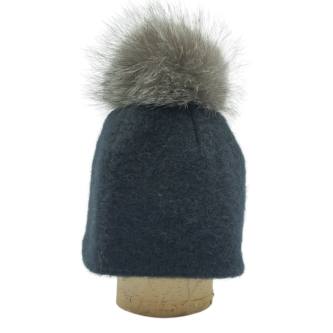 Tuque en laine islandaise noire avec un pompom gris sur une bûche par Fourrures audet