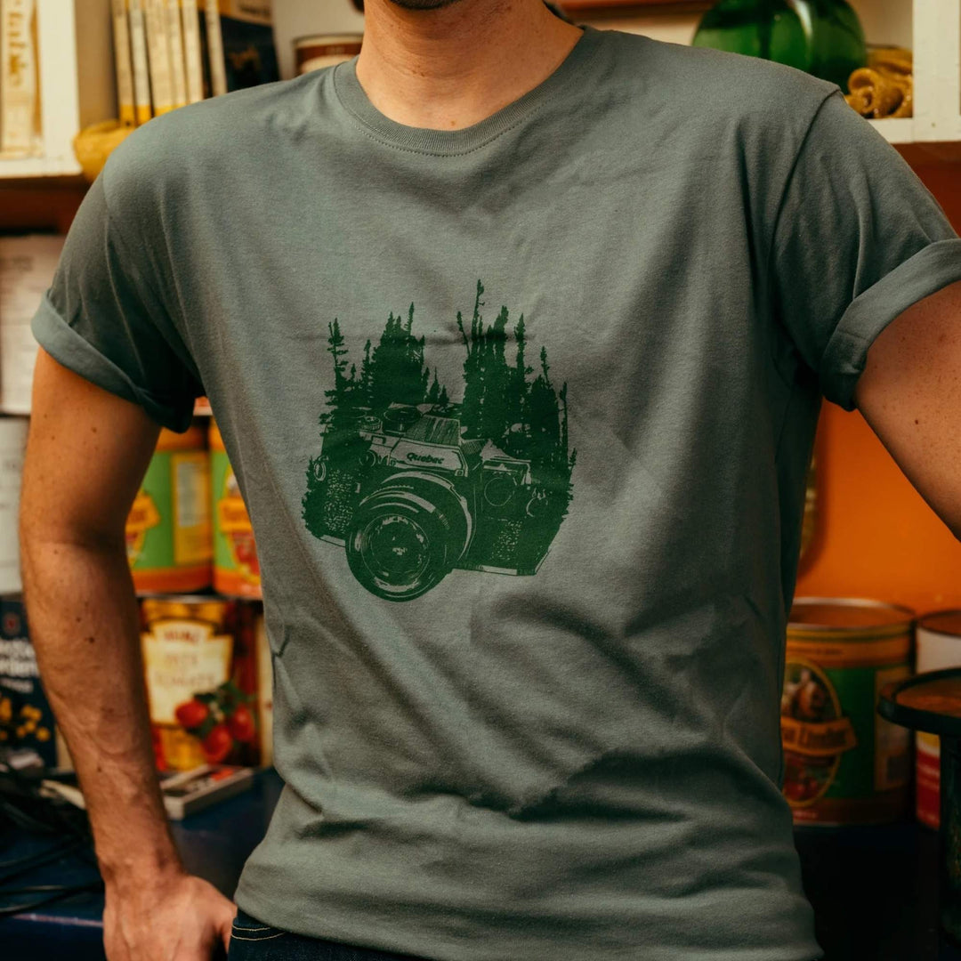 Homme portant un t-shirt vert avec un appareil photo et une forêt en arrière