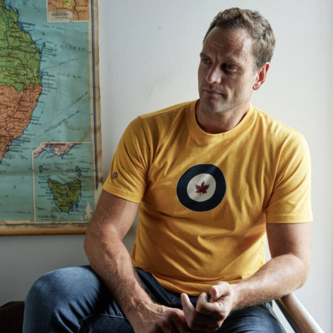 Homme portant un T-shirt RCAF jaune  par Red Canoe regardant au loin avec une carte au mur