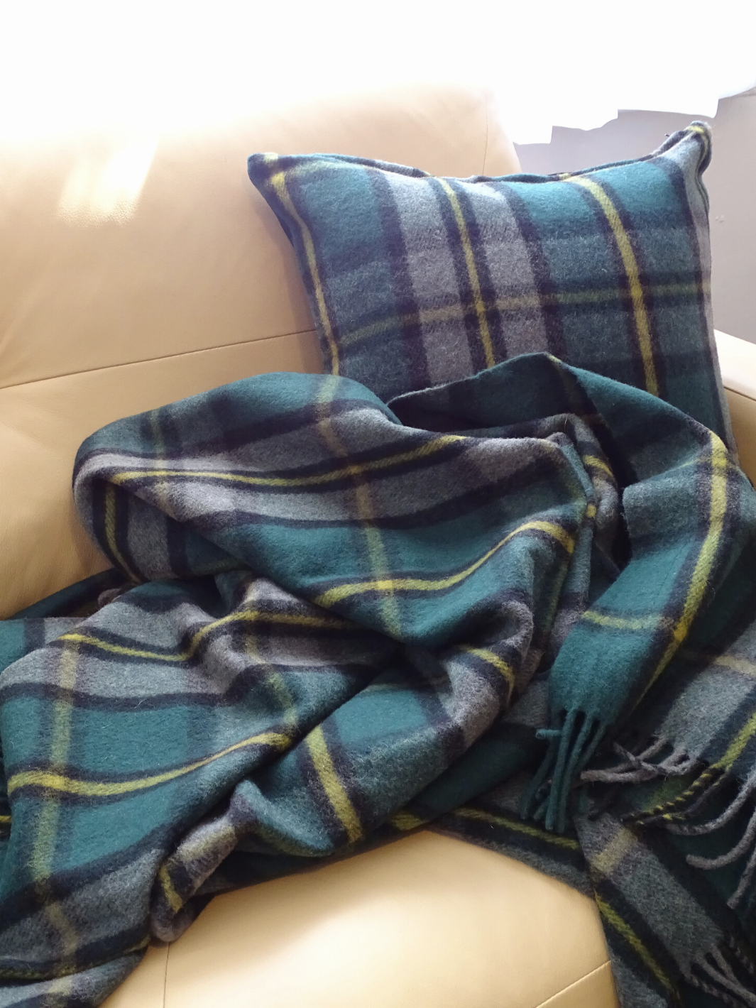 Lourde couverture tartan verte et grise avec fines lignes jaunes sur un divan beige avec coussin tartan assorti