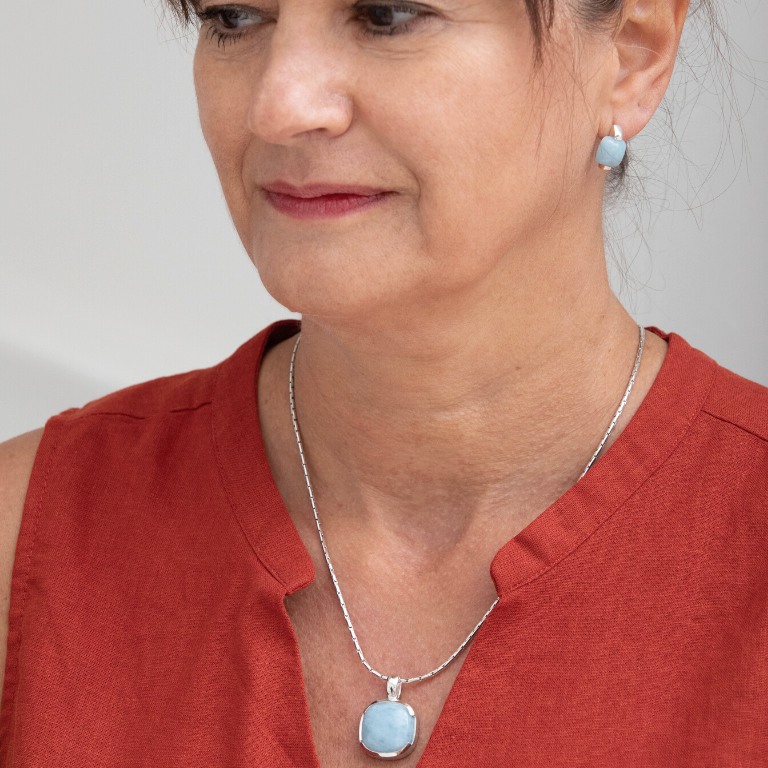 Femme portant une boucle d'oreille bleue de forme carrée avec une chaine argentée et un pendantif bleue