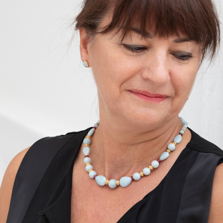 Femme portant une boucle d'oreille ronde de couleur bleue pâle avec un collier assortit de pierres