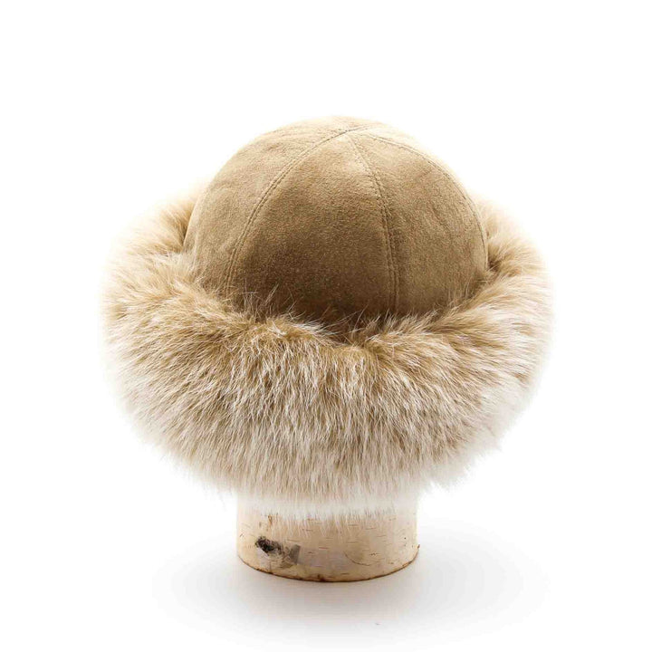 chapeau de fourrure de renard style cloche posé sur une buche de bouleau. Le cuir suède est de couleur beige et la fourrure de renard est beige pâle.