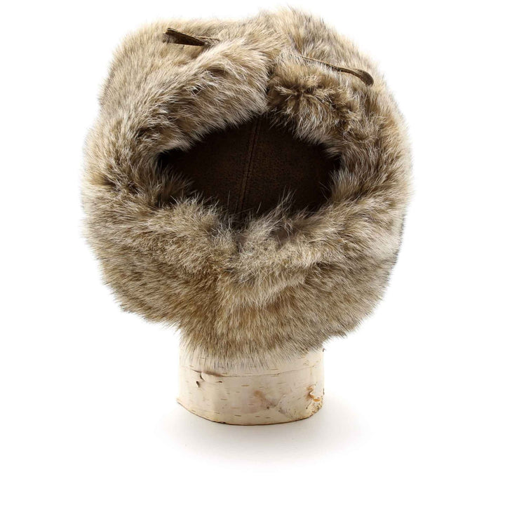 chapeau de fourrure de lynx avec cuir couleur brun posé sur une buche de bouleau et vue de derrière avec les oreilles attachées sur le dessus.