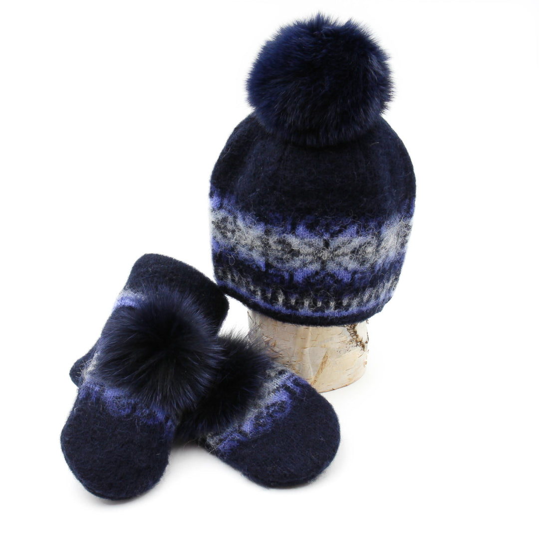 Tuque et mitaines en laine islandaise marine et bleue pâle avec pompom bleu marine déposées sur une buche