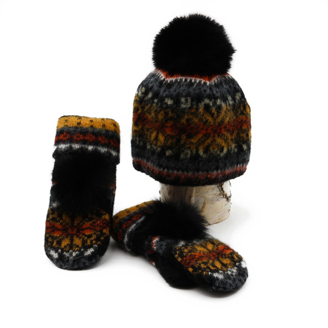 Tuque et mitaines en laine islandaise noire et orange avec un pompom noir déposées sur une buche