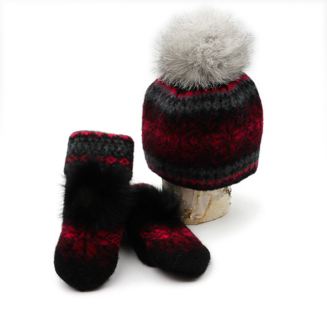 Tuque et mitaines en laine islandaise noire,rouge et grise avec un pompom gris déposées sur une buche