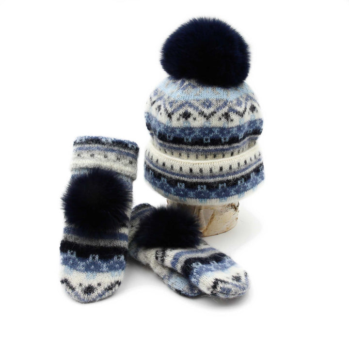Tuque et mitaines en laine islandaise blanches,bleues marines et bleues pâles avec pompom marine déposées sur une buche