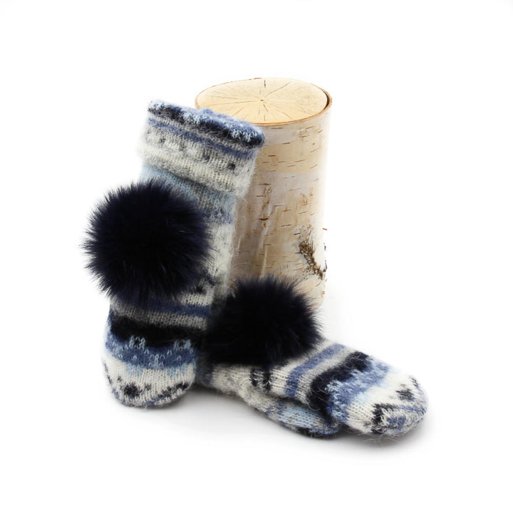 Mitaines en laine islandaise blanches, bleue pâle et marines avec un pompom bleu marine sur le dessus déposée sur une buche
