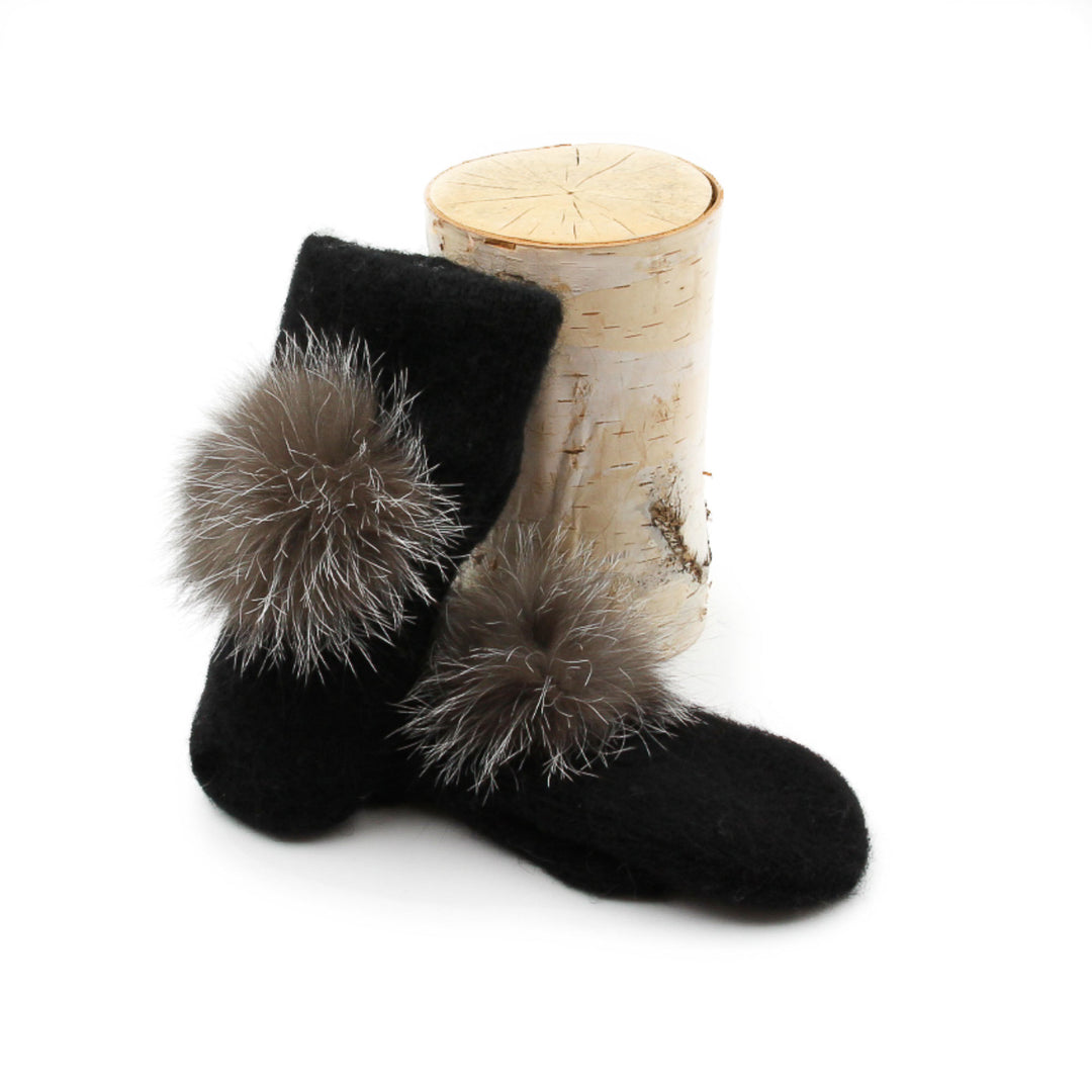 Mitaines en laine islandaise noires avec pompom gris sur le dessus déposées contre une buche