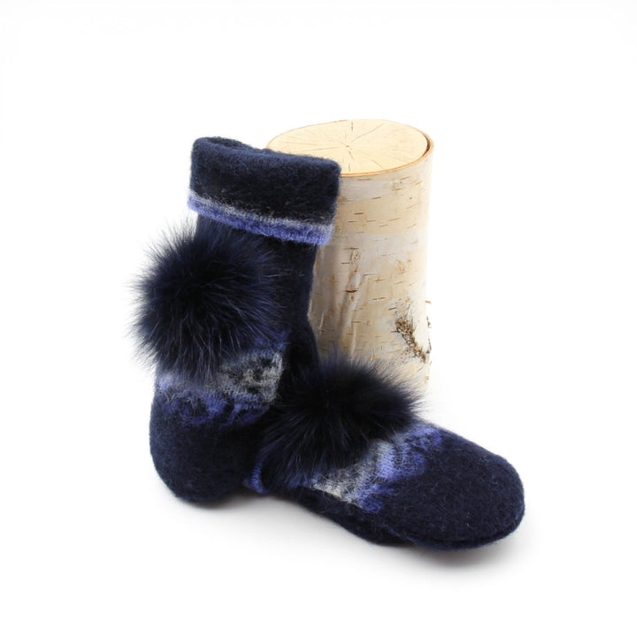 Mitaines en laine islandaire bleues marines et bleues pâles avec pompom marine sur le dessus déposées contre une buche
