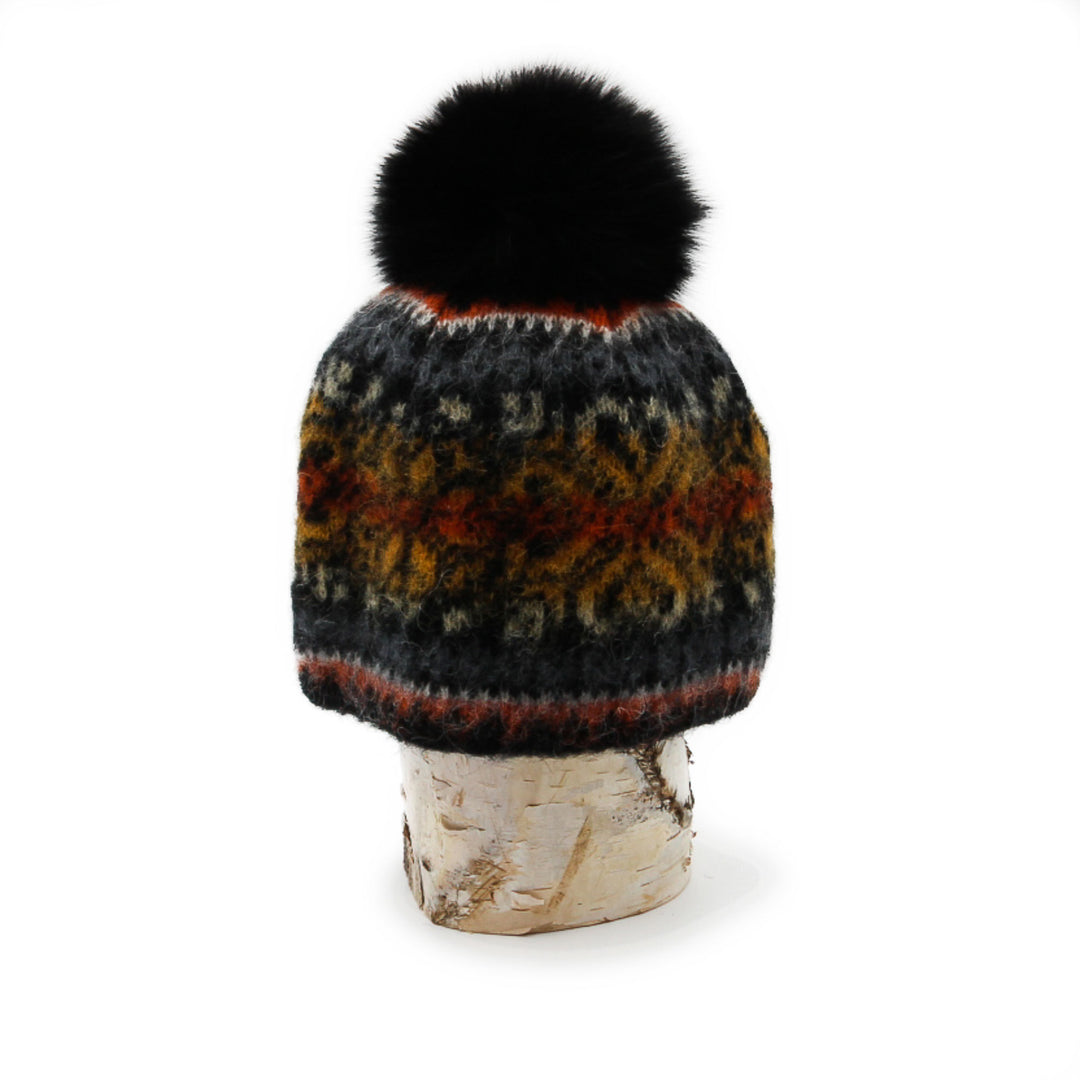 Tuque en laine islandaise grise,noire, orange avec un pompom noir déposée sur une buche