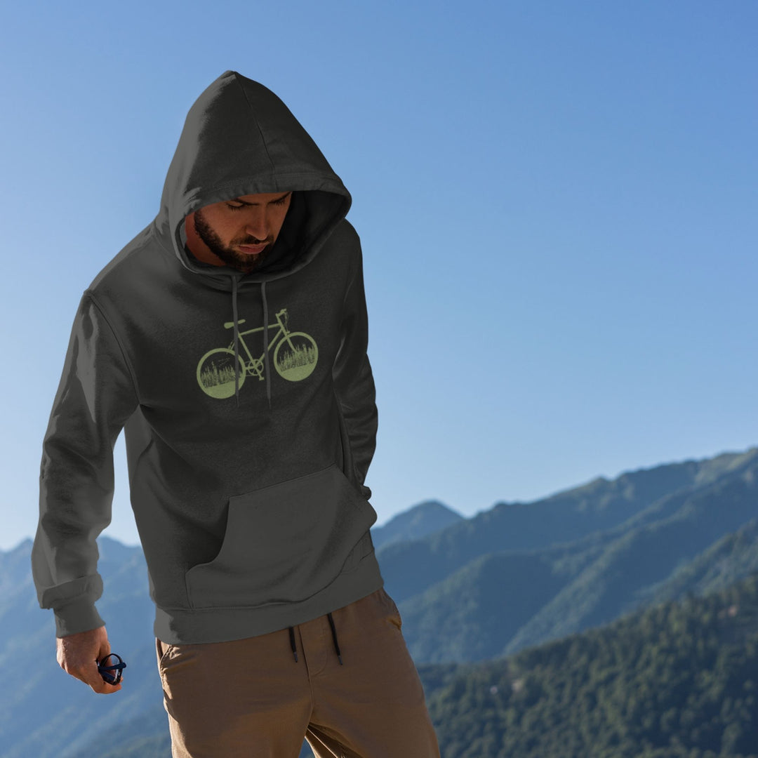 homme sur une montagne qui regarde le sol et qui porte un coton ouaté avec capuchon charcoal. Le coton ouaté a une illustration verte d'une vélo avec les roues  qui sont pleines d'arbres et de conifères.