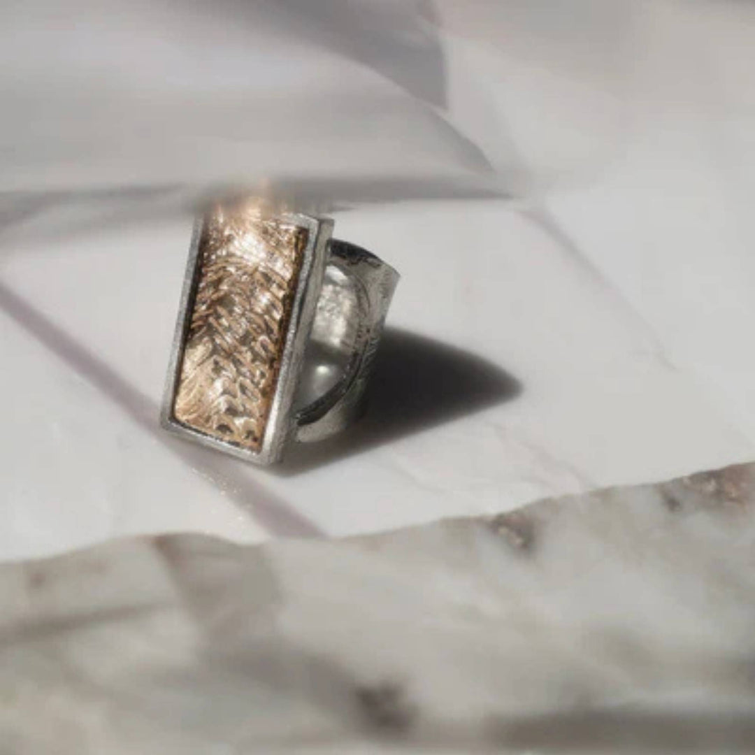 Bague rectangulaire en étain avec dessus doré déposée sur une surface