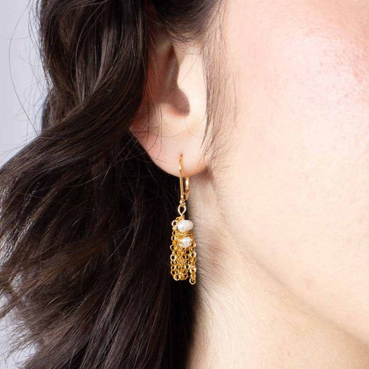 Femme portant une Boucle d'oreilles anne-marie Chagnon Cabaey dorée avec chaîne suspendue et perle