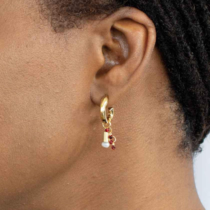 Femme portant une Boucle d'oreilles Anne-Marie Chagnon Jaber avec anneaux dorés, billes rouges, cylindres dorés et perles