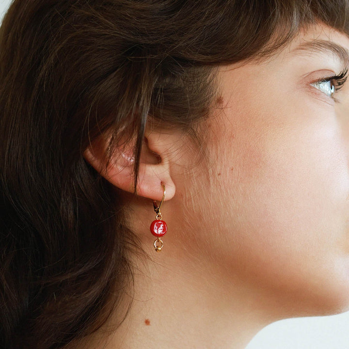 Femme portant une Boucle d'oreilles dorée avec bille rouge suspendue par Anne-Marie Chagnon