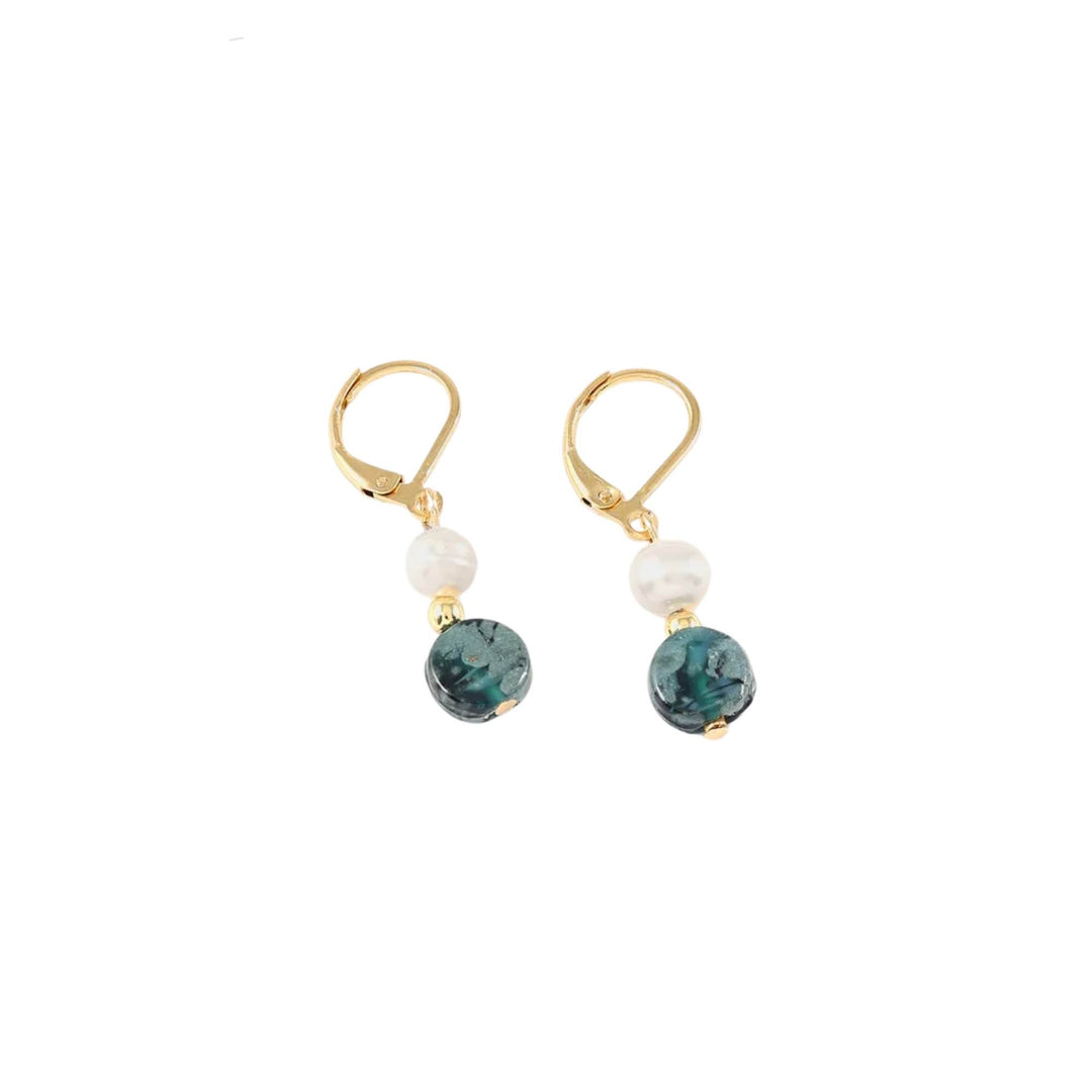 Boucles d'oreilles dorées avec perle et bille turquoise au bout par ANne-Marie Chagnon déposées sur le sol