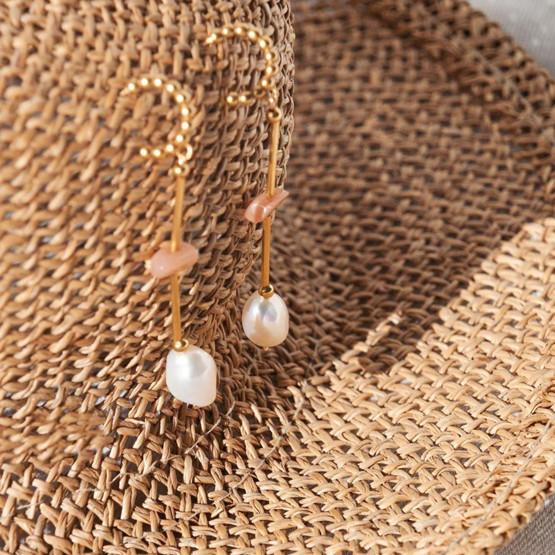 Boucles d'oreilles Welldunn dorées avec perles et pierres de soleil déposées sur un chapeau d'été