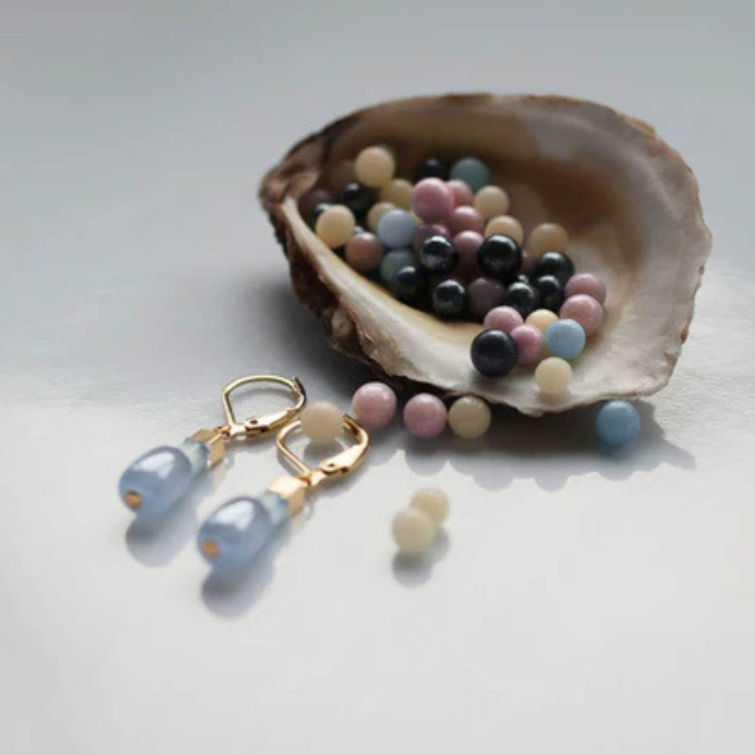 Boucles d'oreilles dorées avec billes bleues par Anne-Marie Chagnon dans un coquillage de perles