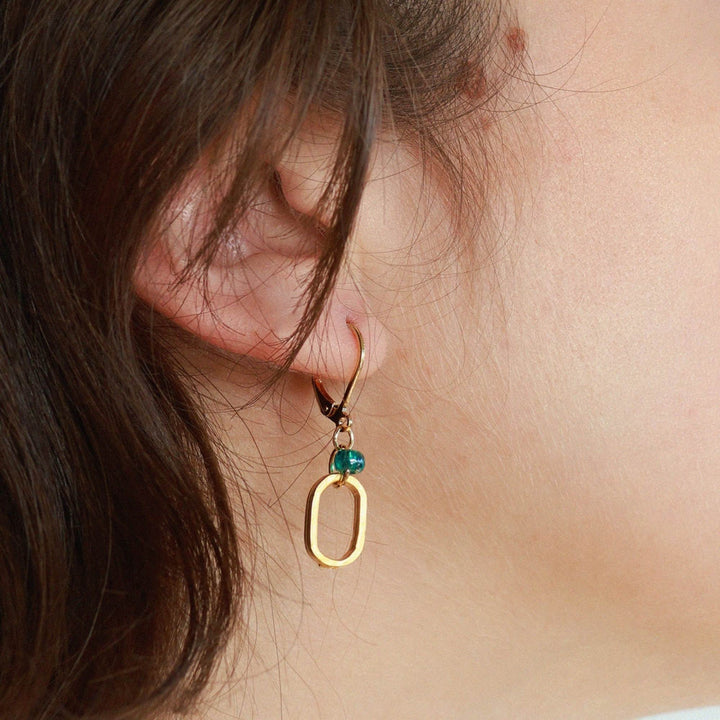 Femme portant une Boucle d'oreilles dorées avec un ovale et une bille turquoise au centre