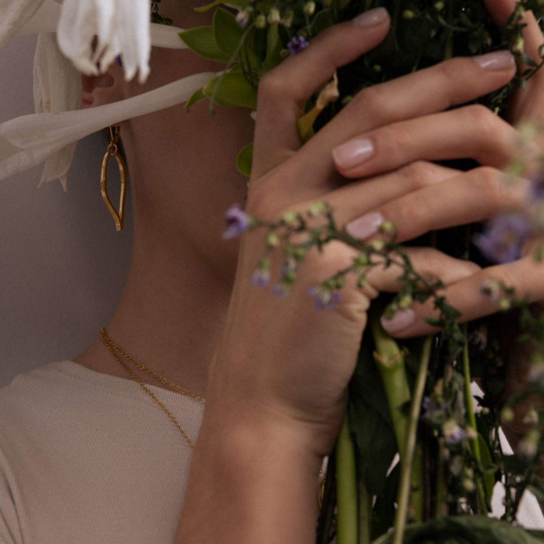 Femme derrière un bouquet de fleurs portant des Boucles d'oreilles ovales dorées par Anne-Marie Chagnon