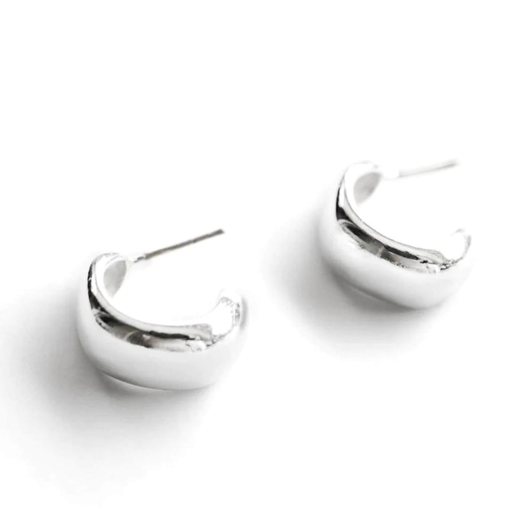 Boucles d'oreilles simples en demi-anneau argenté par welldunn déposées en diagonale sur fond blanc