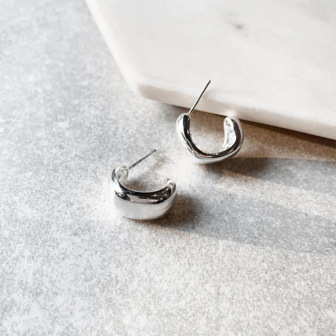 Boucles d'oreilles simples en demi-anneau argenté par welldunn déposées une à côté de l'autre