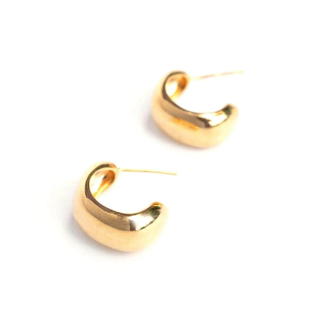 Boucles d'oreilles simple en demi-anneau doré par welldunn déposées en diagonale sur fond blanc