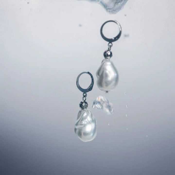 Boucles d'oreilles argentées avec bille de verre blanche au bout par ANne-Marie Chagnon dans l'eau