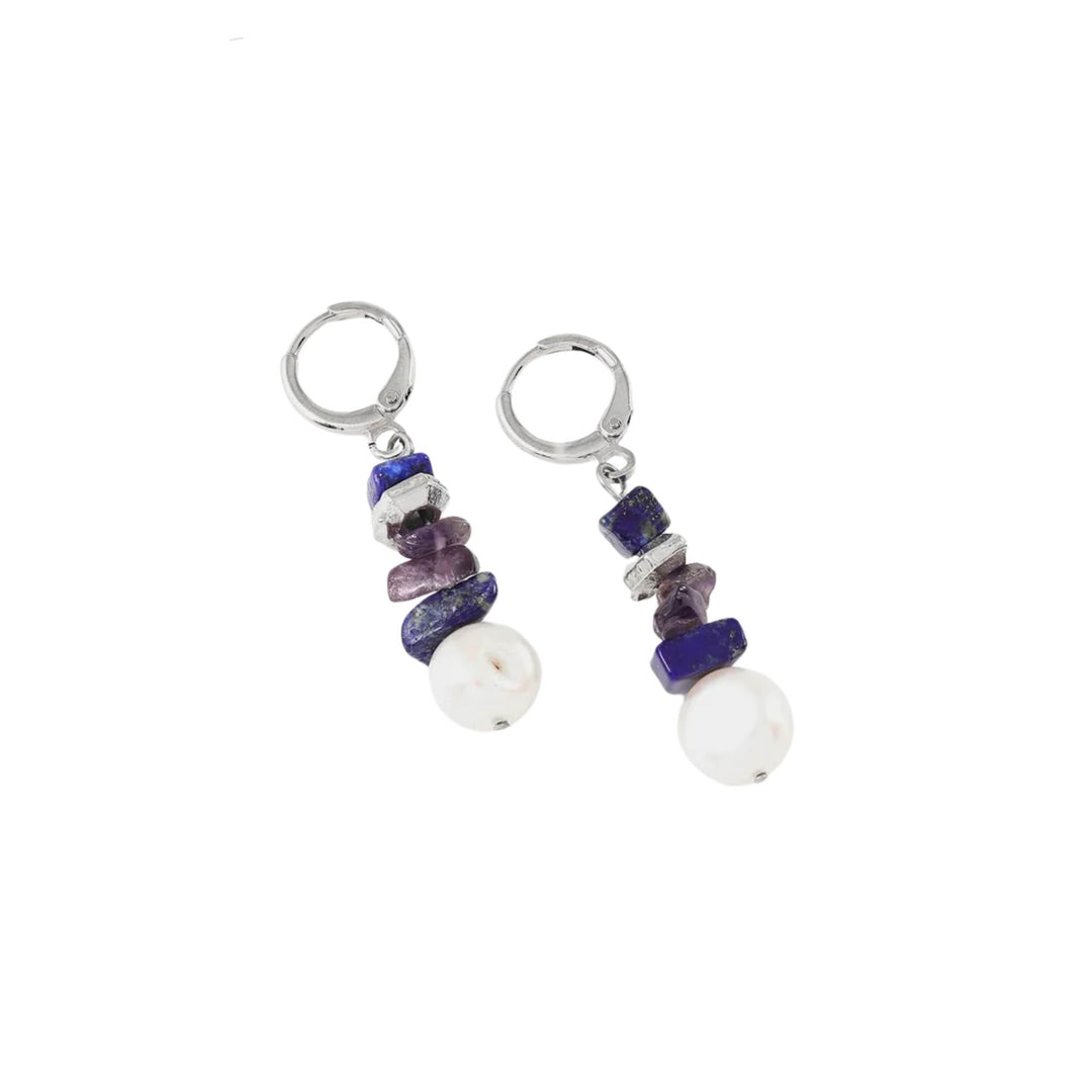 Boucles d'oreilles bleues et mauves avec perle suspendue par ANne-Marie Chagnon déposées sur une surface