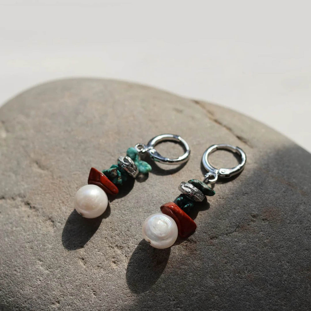 Boucles d'oreilles turquoises et brunes avec perle suspendue par Anne-Marie Chagnon désposées sur une pierre