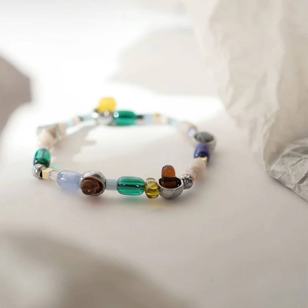 Bracelet avec billes de verre colorées et pièces en étain brut par Anne-Marie Chagnon sur une surface blanche