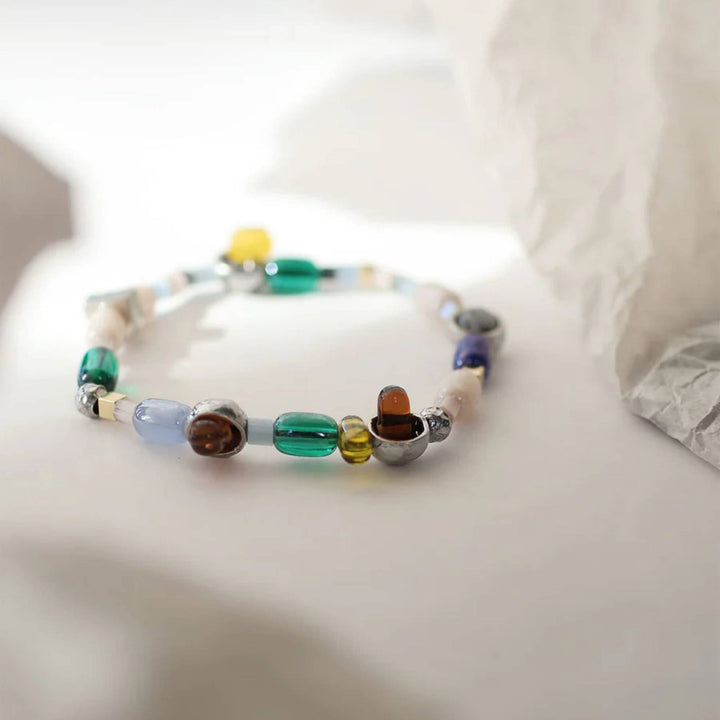 Bracelet avec billes de verre colorées et pièces en étain brut par Anne-Marie Chagnon sur une surface blanche