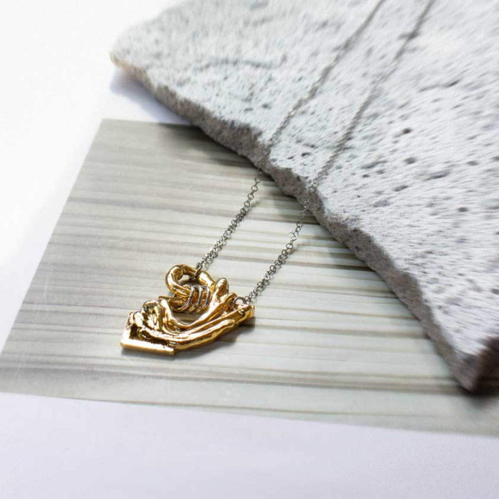 Collier Anne-marie-Chagnon Dougli avec chaîne argentée et pendentif doré déposé sur une pierre