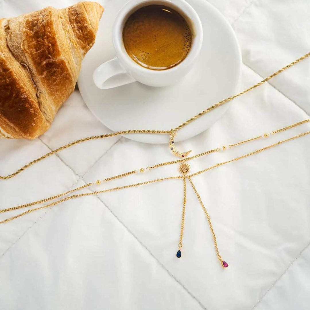 Collier à trois chaînes dorées avec pendentifs de lune, soleil et pierres bleues et rose par welldun avec tasse de café