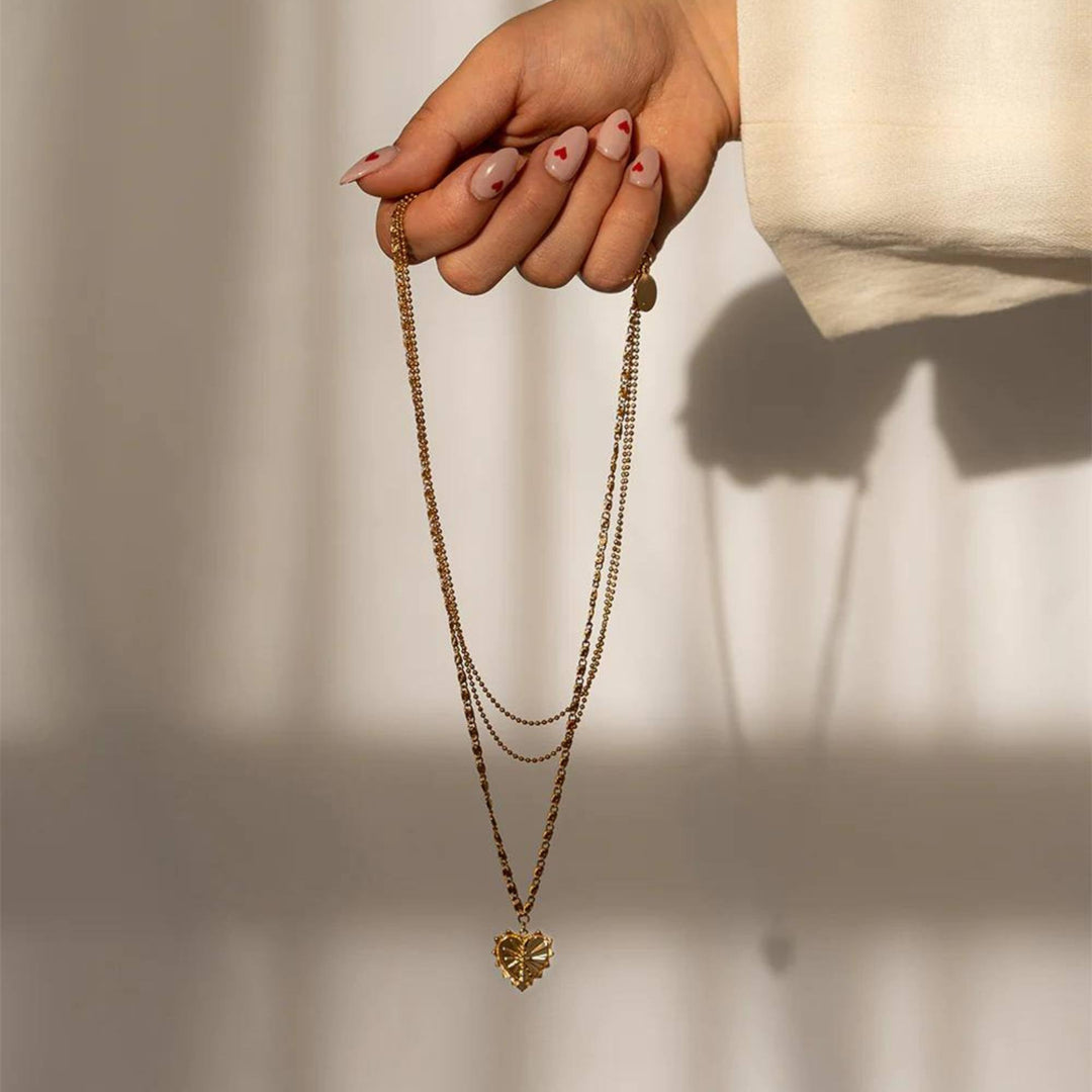 Main tenant un Collier à 3 chaînes doré avec pendentif en coeur par welldunn