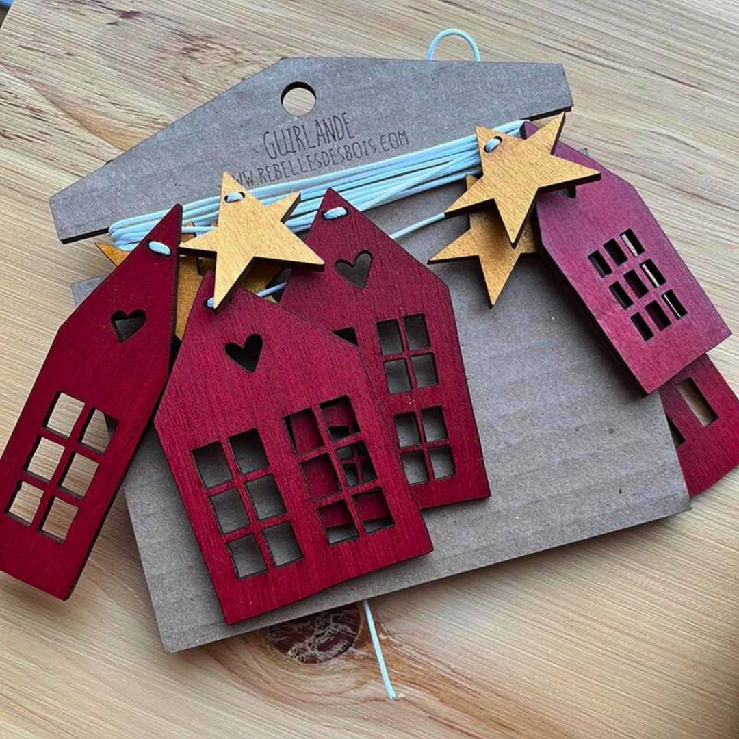 Guirlande en bois scandinaves en forme de maisons rouges et d'étoiles dorées emballée sur du carton par Rebelles des bois