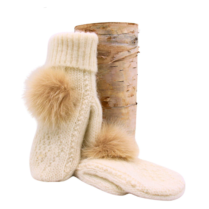 Mitaines blanches en laine avec pompom de fourrure par Fourrures Audet déposées sur une bûche