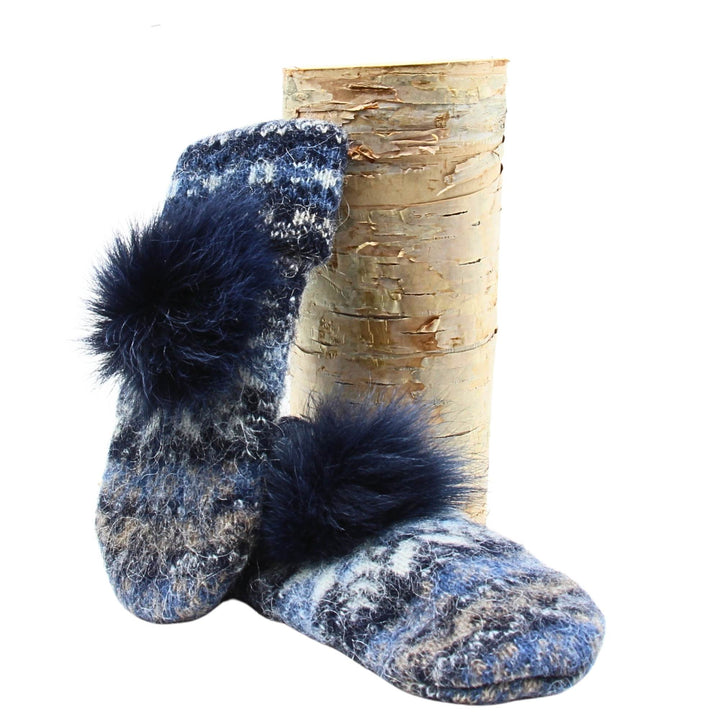 Mitaines en laine islandaise blanches, bleue pâle et marines avec un pompom bleu marine déposée sur une buche