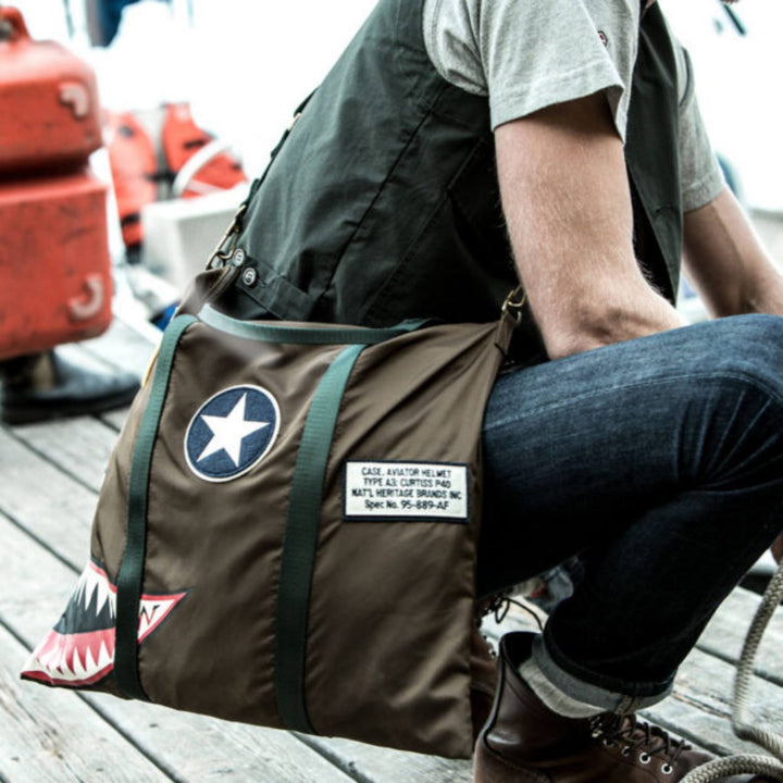 Homme portant un Sac Helmet bag Curstiss P-40 kaki avec poignée par Red Canoe sur un quaie
