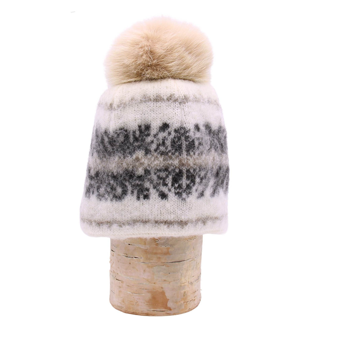 Tuque en laine blanche et grise avec pompom en fourrure de renard sur une bûche par Fourrures Audet