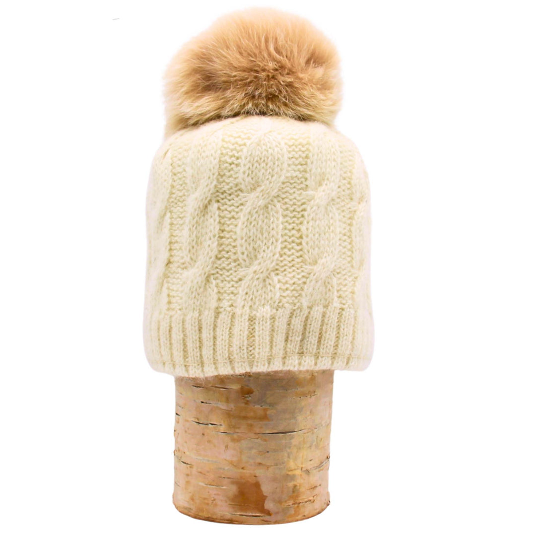 Tuque en laine blanche avec pompom en fourrure de renard sur une bûche par Fourrures Audet