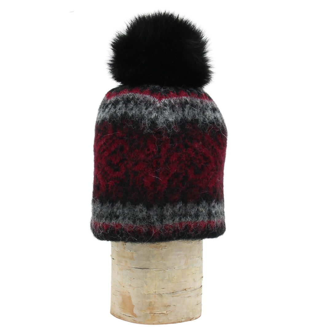 Tuque en laine islandaise noire,rouge et grise avec un pompom noir déposée sur une buche